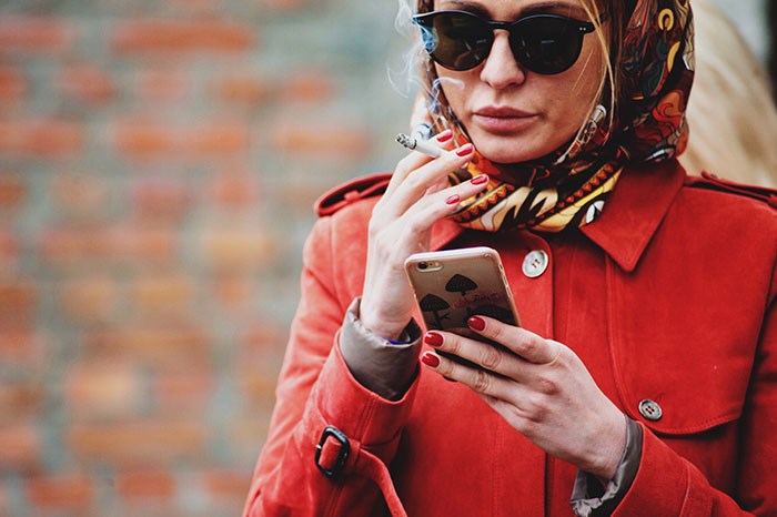 Woman in scarf and red jacket smoking and looking at her phone